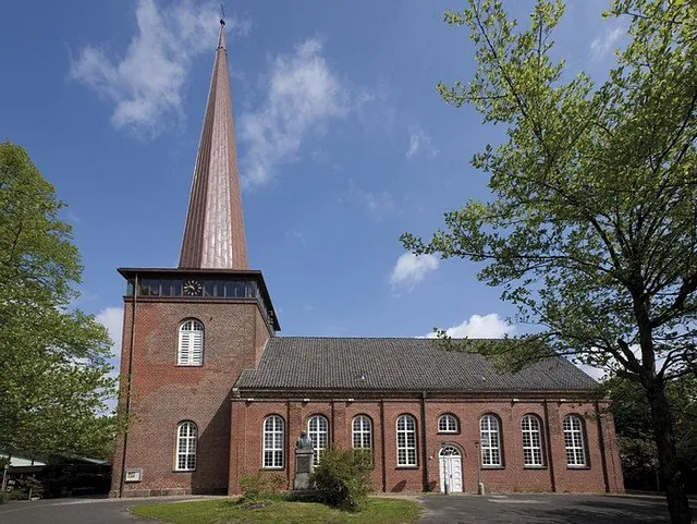 Kirche vor leicht bewölktem Himmel mit Bäumen im Vordergrund.